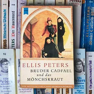 Buchcover 'Bruder Cadfael und das Mönchskraut' vor Buchrücken aller weiteren Bände der Reihe